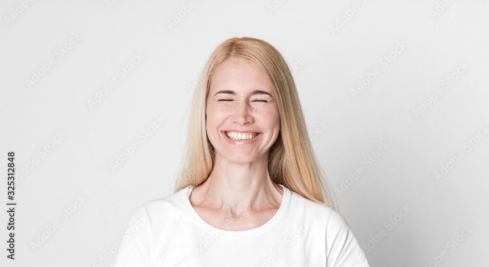Happy middle-aged woman laughing at grey studio Happy middle-aged woman laughing at grey studio