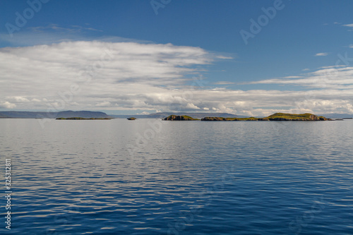 Die Inselgruppe der Flatey Inseln vor Island an einem sonnigen Tag mit spiegelglatter Meeresoberfl  che unter blauem Himmel