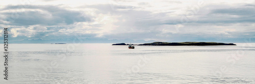 Panorama der spiegelglatten Meeresoberfläche vor Island mit Insel und Schiff an einem hellen Tag