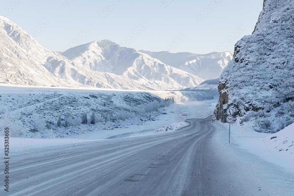winter snowy landscape of a mountain valley with a river with a slippery icy road with steep dangerous turns and road signs