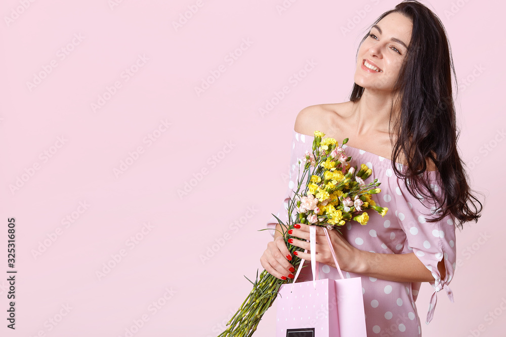 Image of cheerful young brunette lady with long hair being excited to get bouquet of flowers on women's day isolated over rose background, girl looking aside. Copy space for advertisment or promotion. Image of cheerful young brunette lady with long hair being excited to get bouquet of flowers on women's day isolated over rose background, girl looking aside. Copy space for advertisment or promotion.