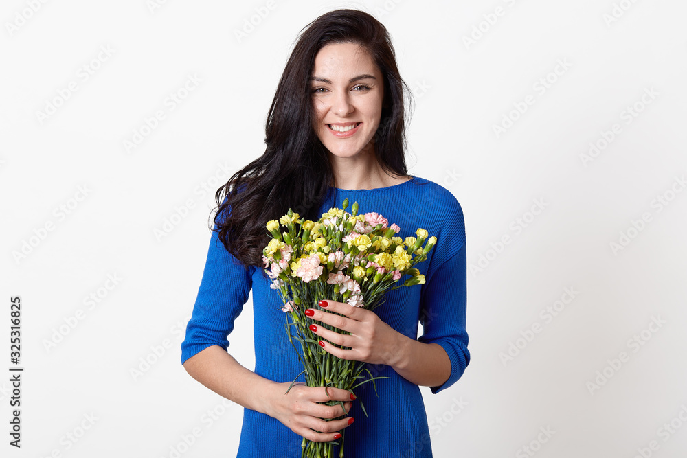 Studio shot of beautiful brunette girl holding bouquet of flowers, attractive woman with big bunch of flowers, dark haired female dressed blue dress, posing over white background, expressing happyness Studio shot of beautiful brunette girl holding bouquet of flowers, attractive woman with big bunch of flowers, dark haired female dressed blue dress, posing over white background, expressing happyness