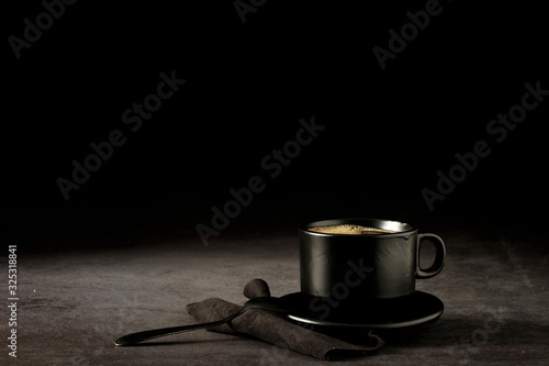 Black coffee cup with coffee on a dark background. With copy space for your text. Cup of coffee on a black background low key copy space.