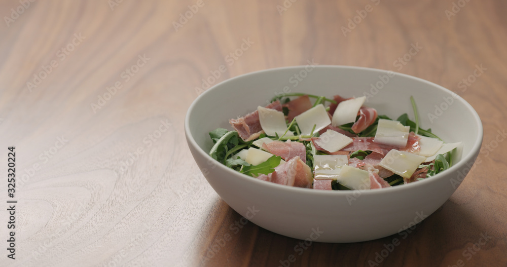 salad with arugula, prosciutto and cherry tomatoes in white bowl on walnut table salad with arugula, prosciutto and cherry tomatoes in white bowl on walnut table