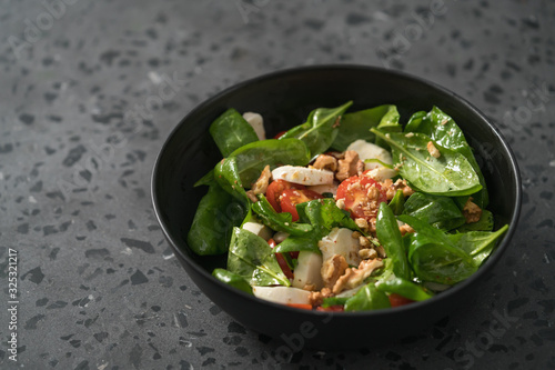 Salad with spinach, tomatoes and mozzarella in black bowl on concrete countertop with copy space