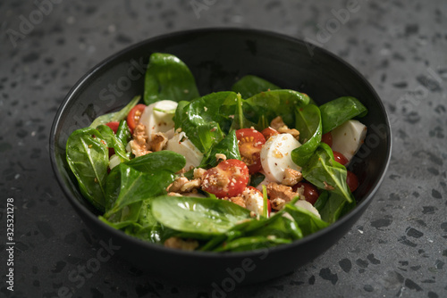 Salad with spinach, tomatoes and mozzarella in black bowl on concrete countertop