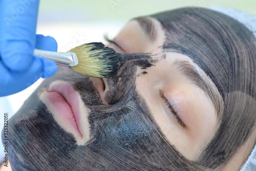 Cosmetologist beautician applying carbon nanogel to skin of woman face using brush. Beautician making preparation procedure carbon peeling with laser rejuvenation in beauty clinic, closeup portrait. photo