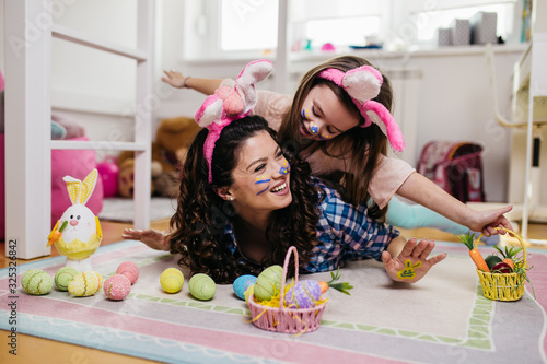 Mother and her cute little daughter playing in children's room while preparing Easter decoration.