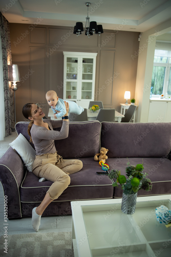 Obraz premium Smiling young beautiful lady resting with her kid at home