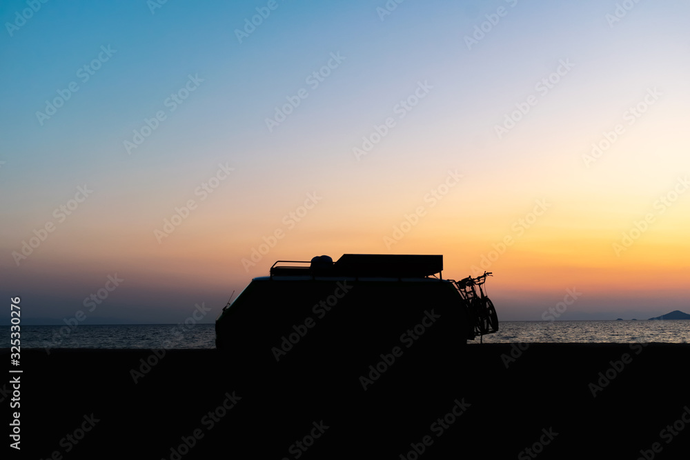 Fototapeta premium Motorhome silhouette on the beach in the sunset Beautiful orange sky color and calm sea in the background. Camper van lifestyle