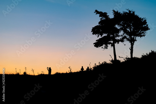 Silhouettes of people walking over the hill in beautiful colorful sunset. Outdoor activities