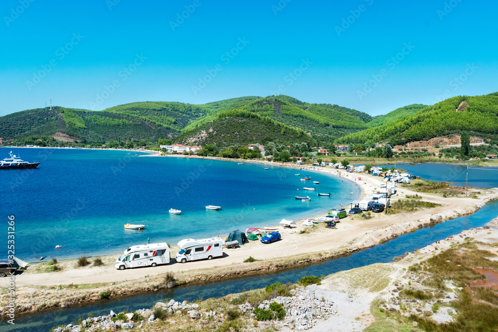 View on famous Greek bay with many recreational vehicles parked around the beach and turquoise blue water. Perfect vacation place for camping lifestyle.
