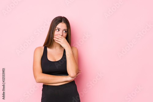 Young fitness caucasian woman isolated thoughtful looking to a copy space covering mouth with hand.