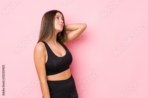 Young fitness caucasian woman isolated touching back of head  thinking and making a choice.