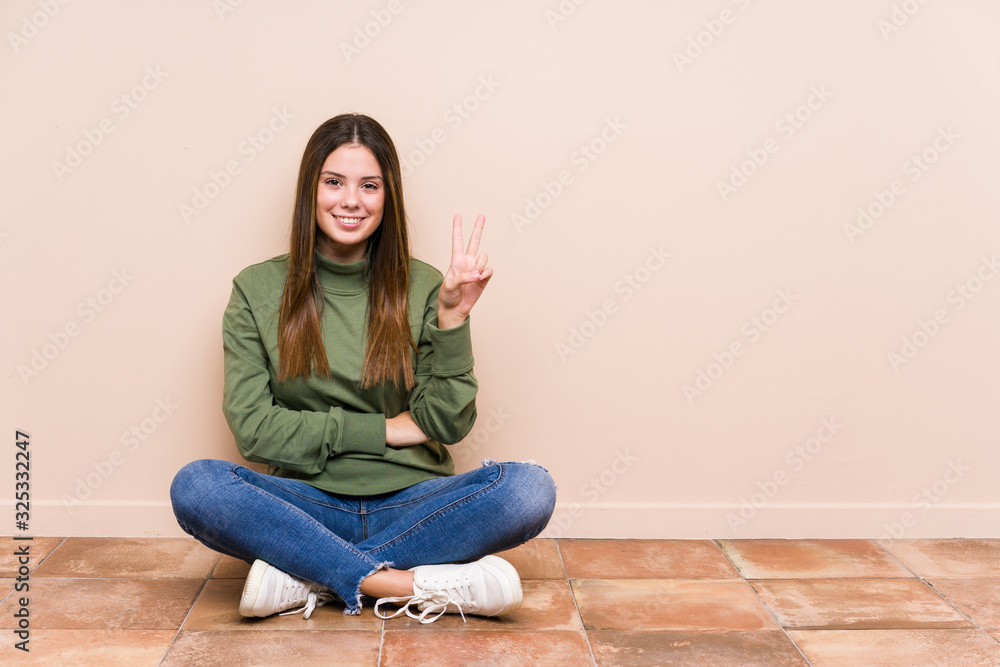 Young caucasian woman sitting on the floor isolated showing number two with fingers. Young caucasian woman sitting on the floor isolated showing number two with fingers.