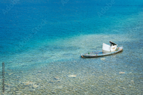 Old forgotten wooden boat rotting in the shallow turquoise waters of the bay. Transparent blue water with rocks on the bottom.