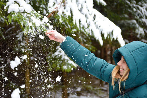 Happy blond girl playing with the snow on the conifer tree in the forest during winter