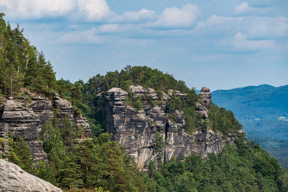 Naklejka premium Pravcicka brana in Bohemian Switzerland. Prebischtor Gate mountain view. Narrow rock, largest natural sandstone arch in Europe. Hill scenery with greenery, blue sky and sunlight, natural environment.