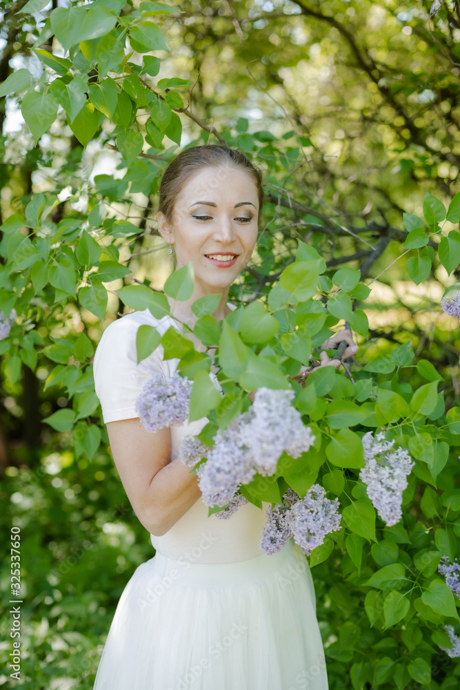 Beautiful girl is walking in the spring park near the trees in bloom. Spring season, sunny weather.