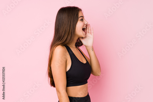 Young caucasian fitness woman doing sport isolated shouting and holding palm near opened mouth. © Asier