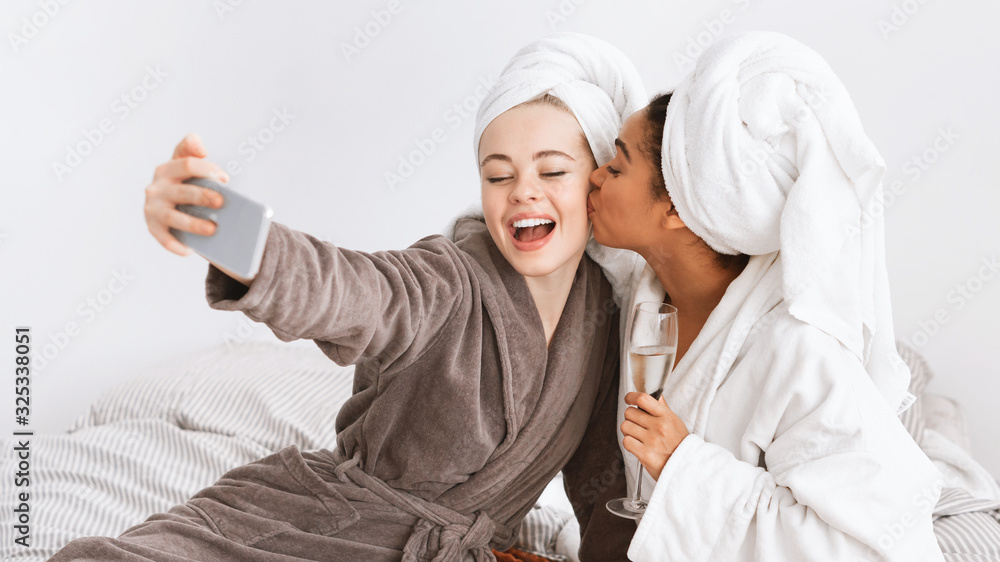 Two ecstatic women taking selfie in bathrobes, drinking champagne Two ecstatic women taking selfie in bathrobes, drinking champagne