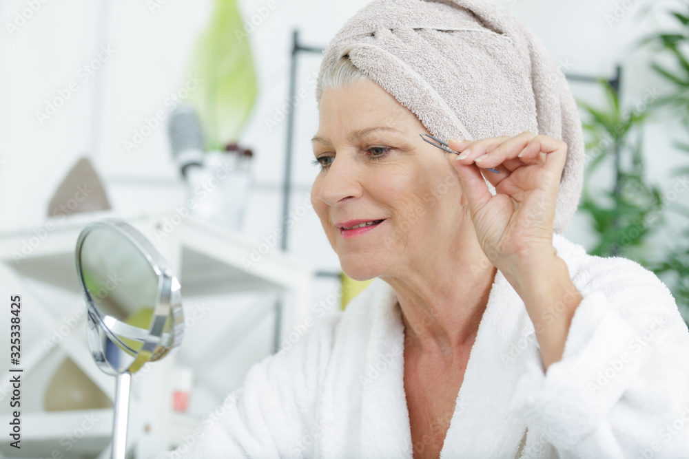 a senior woman plucking her eyebrows with tweezers a senior woman plucking her eyebrows with tweezers