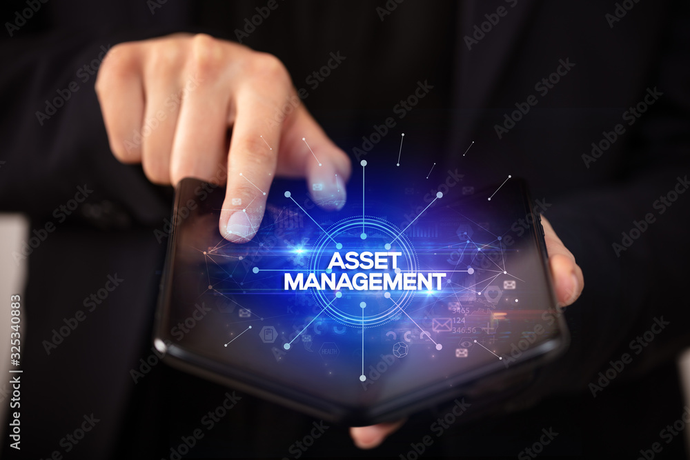 Businessman holding a foldable smartphone with ASSET MANAGEMENT inscription, new business concept Businessman holding a foldable smartphone with ASSET MANAGEMENT inscription, new business concept