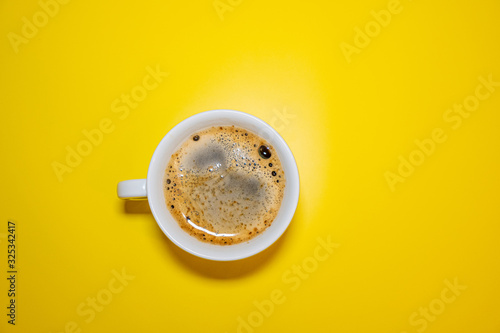 White coffee Cup with foam on a bright yellow background top view, minimalism concept