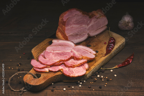 Sliced smoked pork meat with spices lies on an ancient cutting Board on a wooden rustic table against a dark background. Focus concept