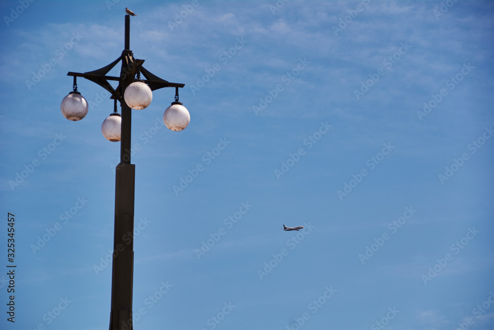 The lamppost looking at the plane in blue sky The lamppost looking at the plane in blue sky