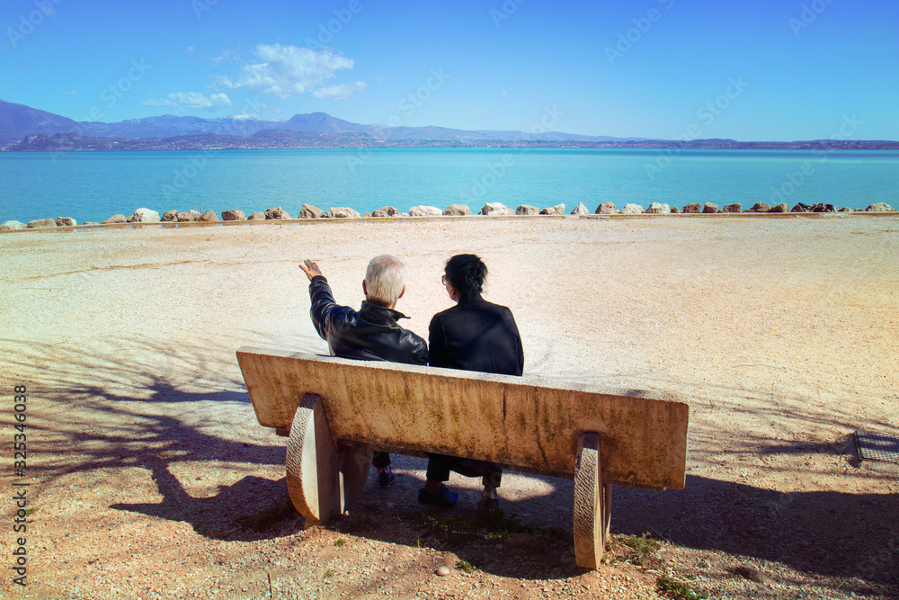 couple sitting by the lake, man indicates something to the woman