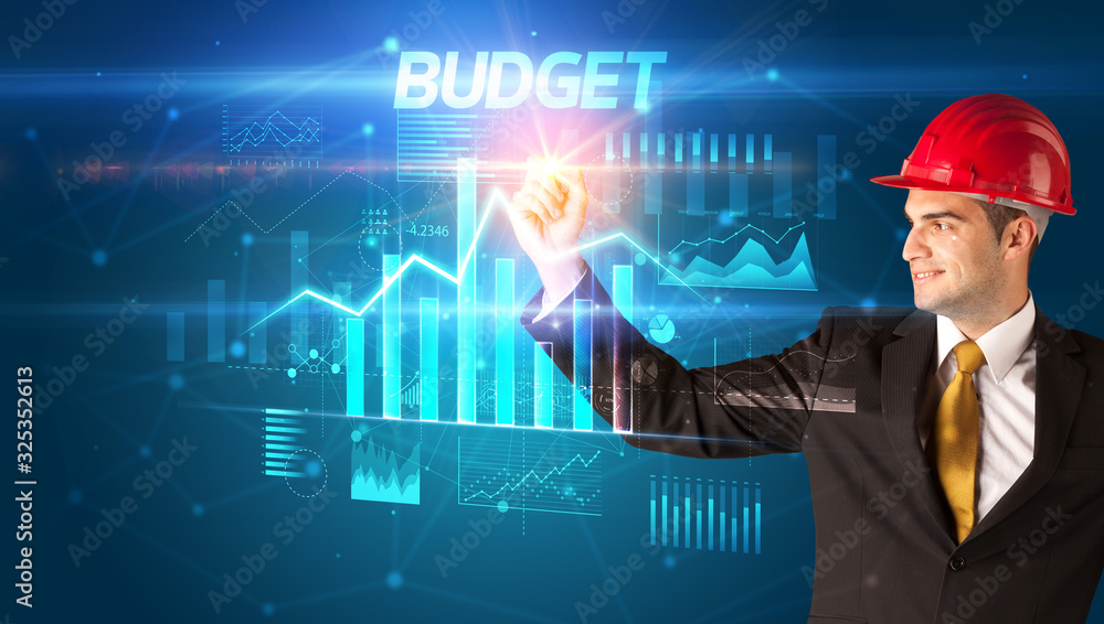 Handsome businessman with helmet drawing BUDGET inscription, architecture business plan concept Handsome businessman with helmet drawing BUDGET inscription, architecture business plan concept