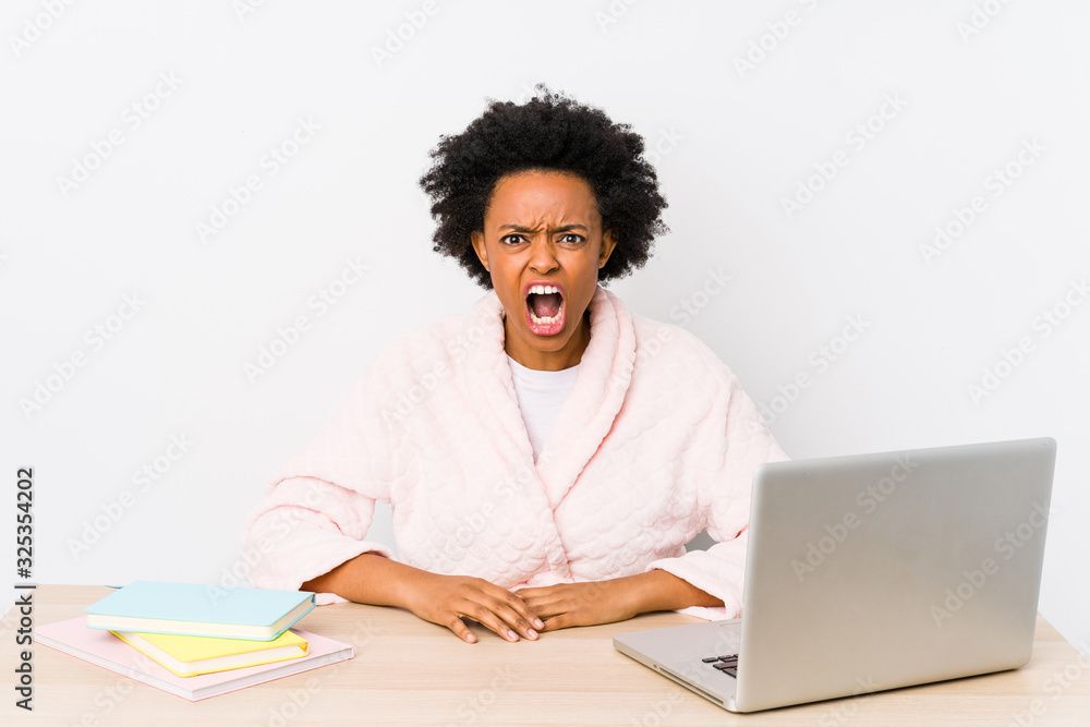 Middle aged african american woman working at home isolated screaming very angry and aggressive. Middle aged african american woman working at home isolated screaming very angry and aggressive.