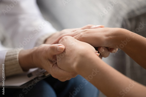 Close up middle aged female doctor holding hands of girl patient.