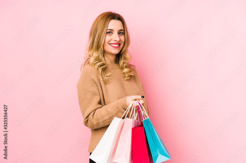 Young blonde woman holding shopping bags isolated looks aside smiling, cheerful and pleasant.