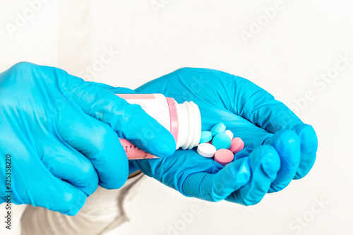 Close-up of hands in blue medical gloves holding a bottle with multi-colored pills. The doctor gives a dose of medication or vitamins and antibiotics to treat health for patient in the palm of hand.