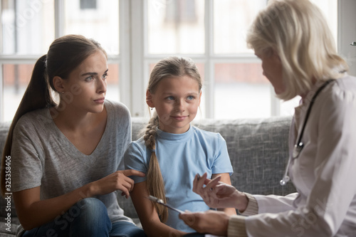 Serious young mother with school daughter attending mature pediatrician.