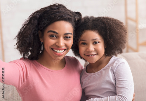 Young afro mother and her cute little daughter taking selfie together