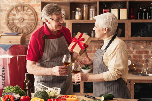 Romantic senior couple exchanging gifts and drinking wine in kitchen