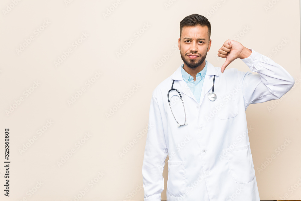 Young south-asian doctor man showing a dislike gesture, thumbs down. Disagreement concept. Young south-asian doctor man showing a dislike gesture, thumbs down. Disagreement concept.