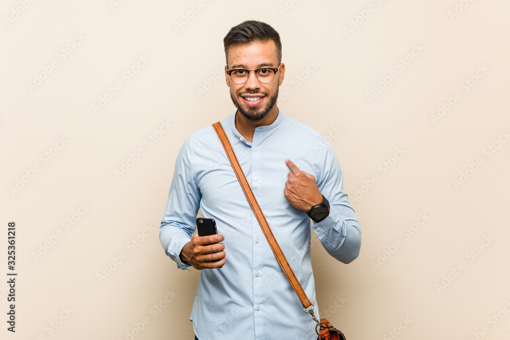Young mixed race asian business man holding a phone surprised pointing at himself, smiling broadly. Young mixed race asian business man holding a phone surprised pointing at himself, smiling broadly.