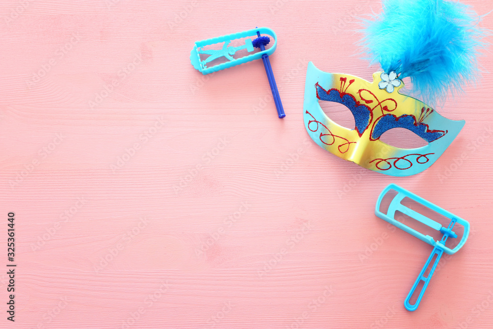 Party colorful noisemaker, mask and cute clown doll over pink wooden background. Top view, flat lay