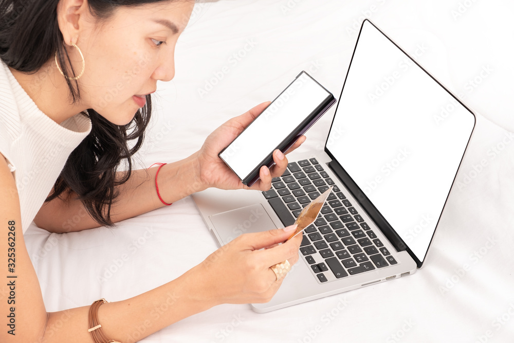 Asian woman using a mobile phone and credit card for shopping online. Blank on the laptop and empty space on smart phone Asian woman using a mobile phone and credit card for shopping online. Blank on the laptop and empty space on smart phone
