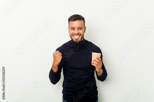 Young mixed race asian man holding a takeaway coffee cheering carefree and excited. Victory concept.