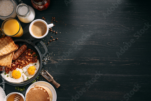 Obraz na płótnie English breakfast on a dark table. fried eggs with bacon canned beans and sausage. near coffee, orange juice and pancakes with butter and honey w salonie