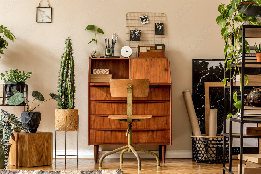 Retro interior design of art workshop room with wooden vintage bureau and  chair, shelf plants, cacti, books, photos and elegant personal accessories.  Stylish vintage home decor. Beige wall. Template. foto de Stock