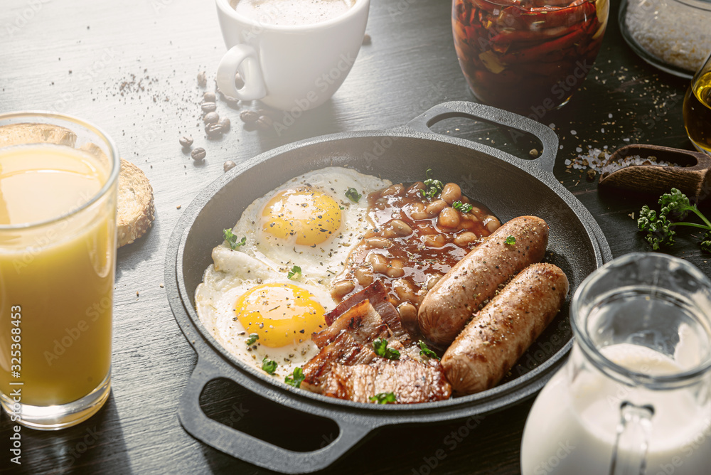 English breakfast on a dark table. fried eggs with bacon canned beans and sausage. near coffee, orange juice and pancakes with butter and honey English breakfast on a dark table. fried eggs with bacon canned beans and sausage. near coffee, orange juice and pancakes with butter and honey