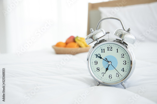 White alarm clock with blur fruits on bed. Eating fruit in the morning will help to excrete well and there is no residue in the intestines.Show time seven o'clock be have wake up to late.