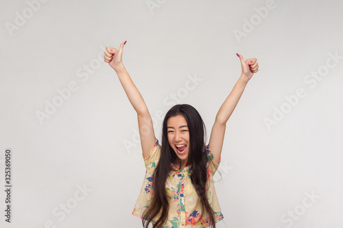 I did excellent job! Delighted pretty asian girl in summer blouse shouting in excitement, raising hands and showing thumbs up, emotionally reacting to victory, success. indoor studio shot isolated