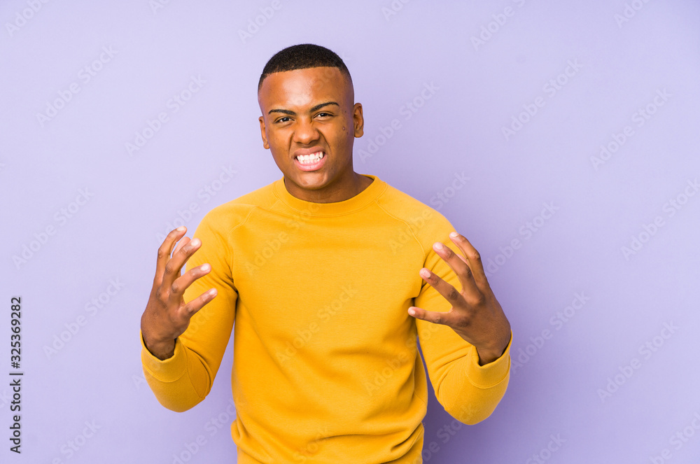 Young latin man isolated on purple background upset screaming with tense hands. Young latin man isolated on purple background upset screaming with tense hands.